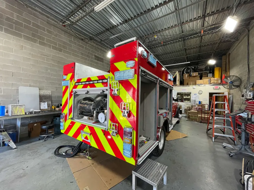Exterior view of small fire truck showing cab, body compartments, and wheel/tire area.